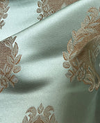Decorative fabric pattern with intricate white designs on a Pista background