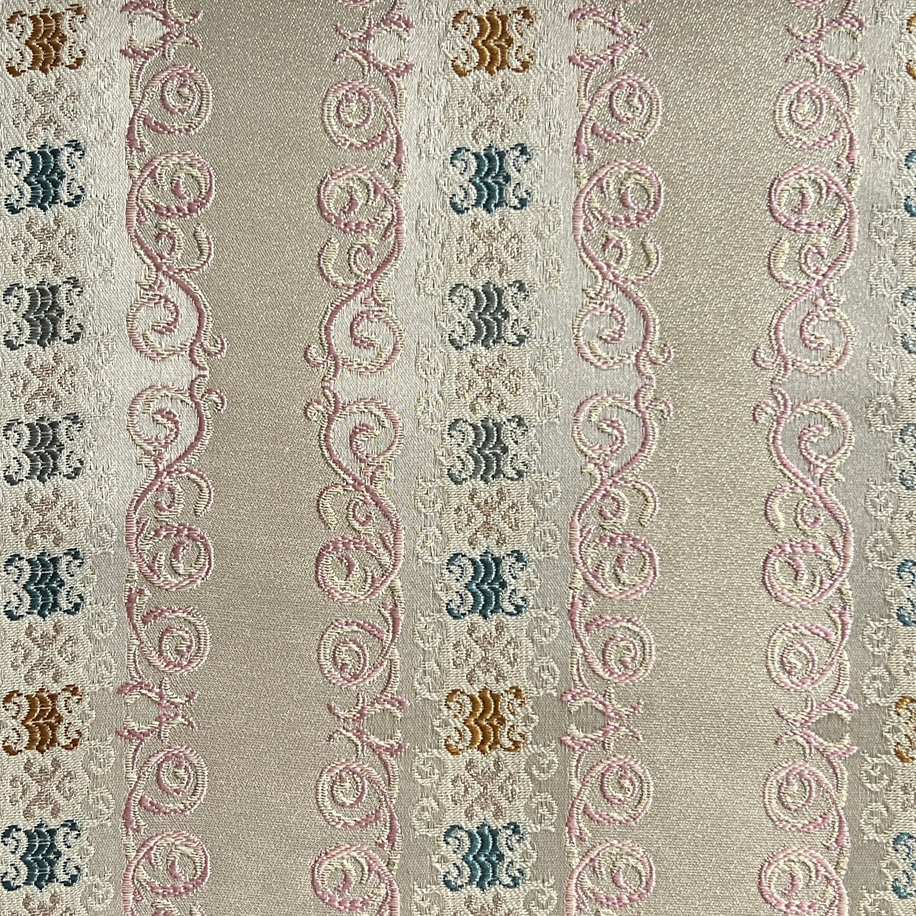 Decorative fabric pattern with intricate designs and color accents on a Pinkish background