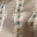 Decorative fabric pattern with intricate designs and color accents on a Pinkish background