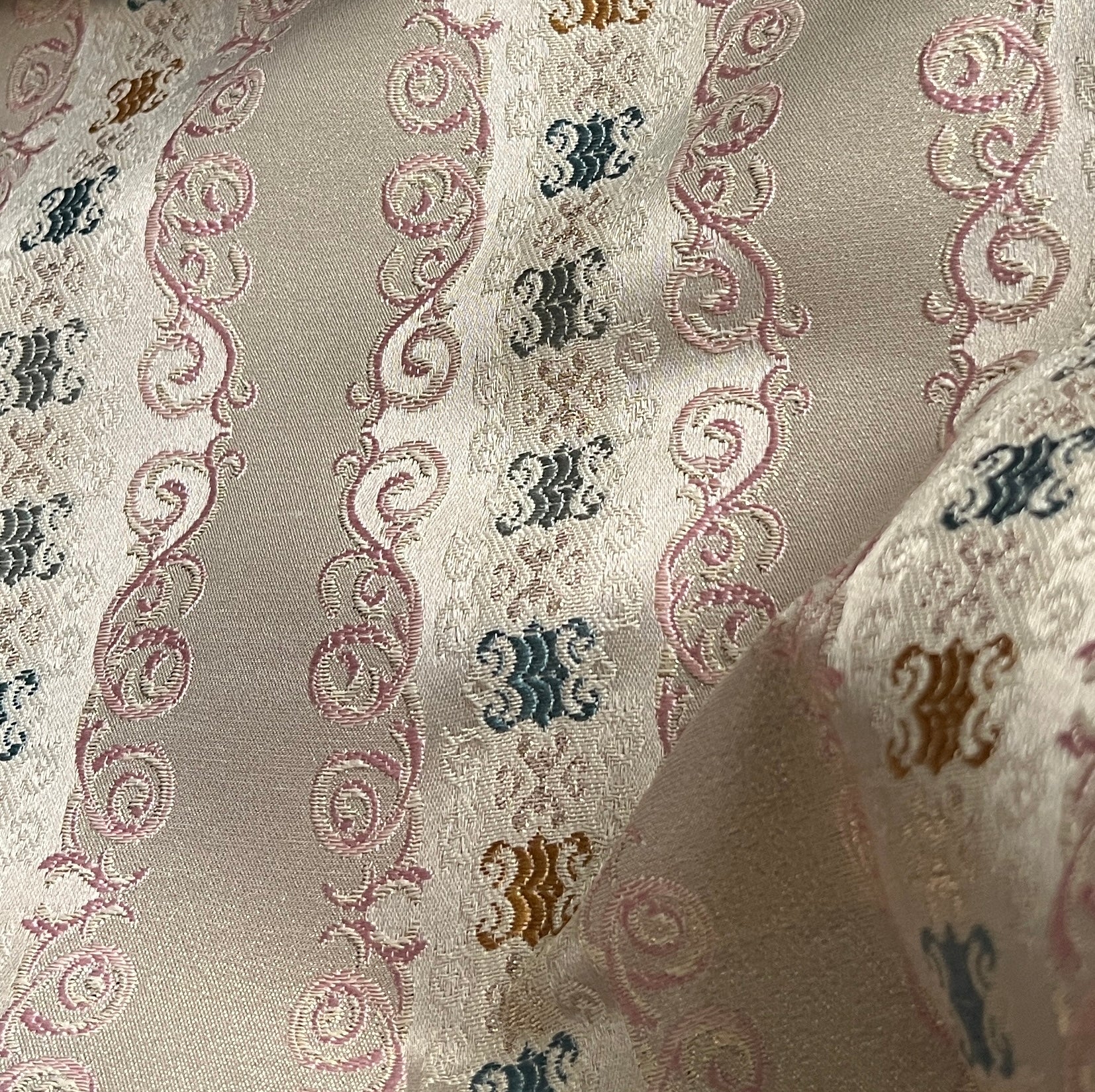 Decorative fabric pattern with intricate designs and color accents on a Pinkish background