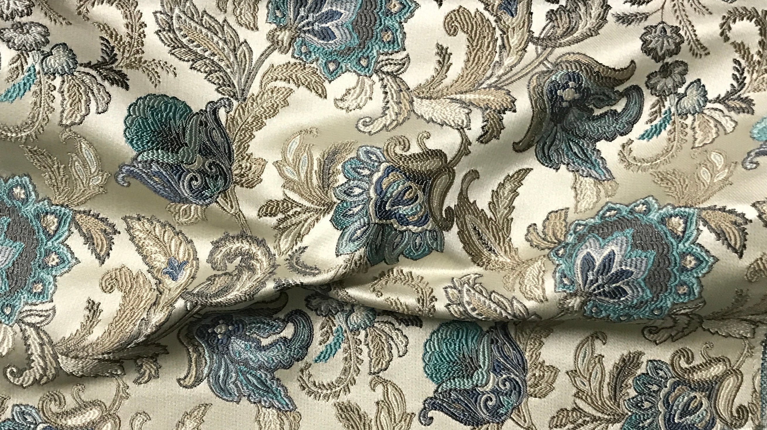 Close-up of decorative fabric with floral patterns in Teal Sage color on a beige background 