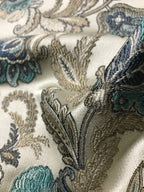 Close-up of embroidered fabric with floral patterns in Teal Sage colors on a white background.