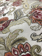 Close-up of embroidered fabric with floral and paisley patterns in a Sage Rose color on a beige background