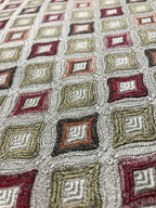 Close-up of a textured fabric with geometric pattern in red, beige, and brown. Sage Rose