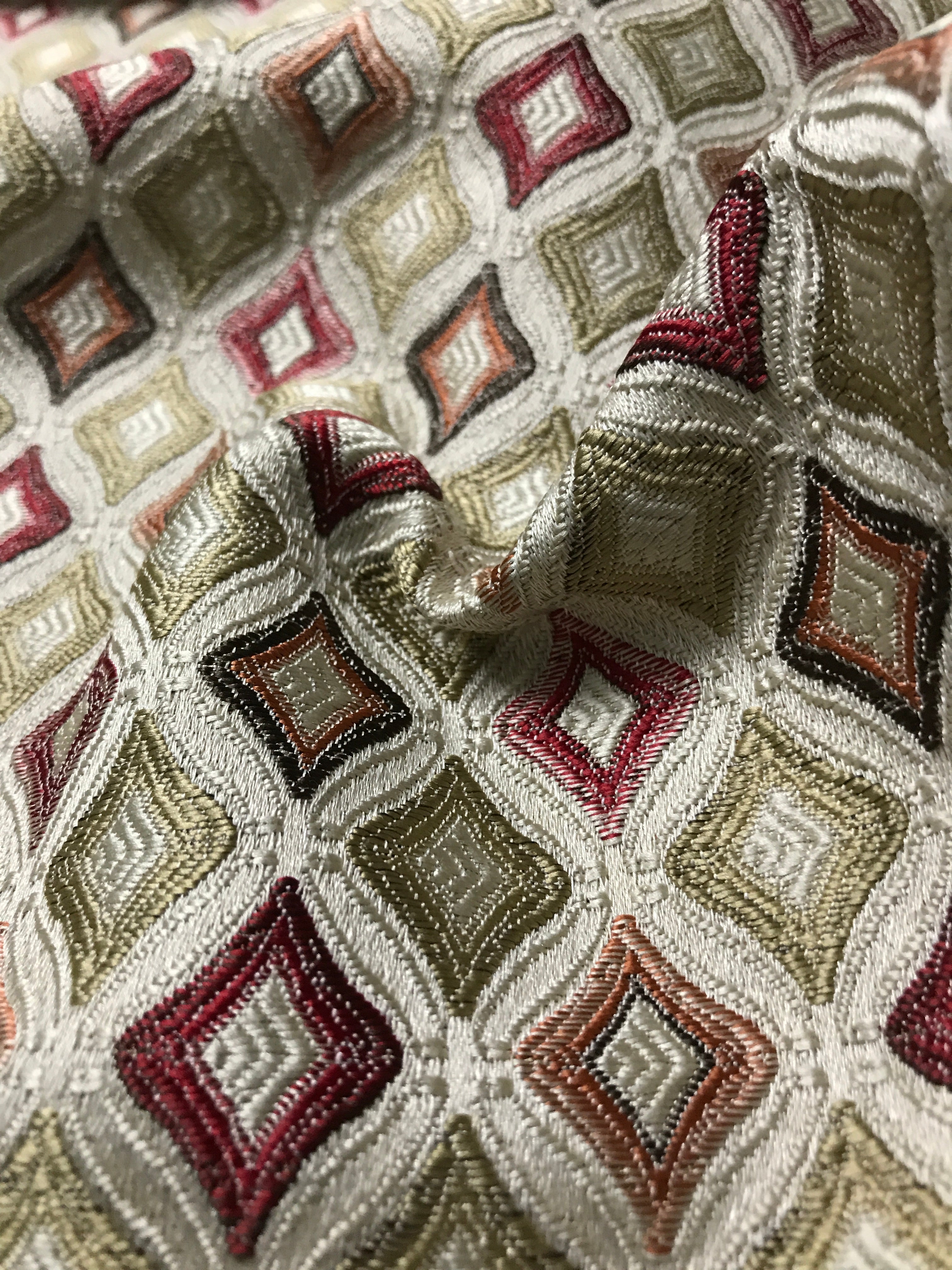 Close-up of patterned fabric with geometric design in red, beige, and brown. Sage Rose