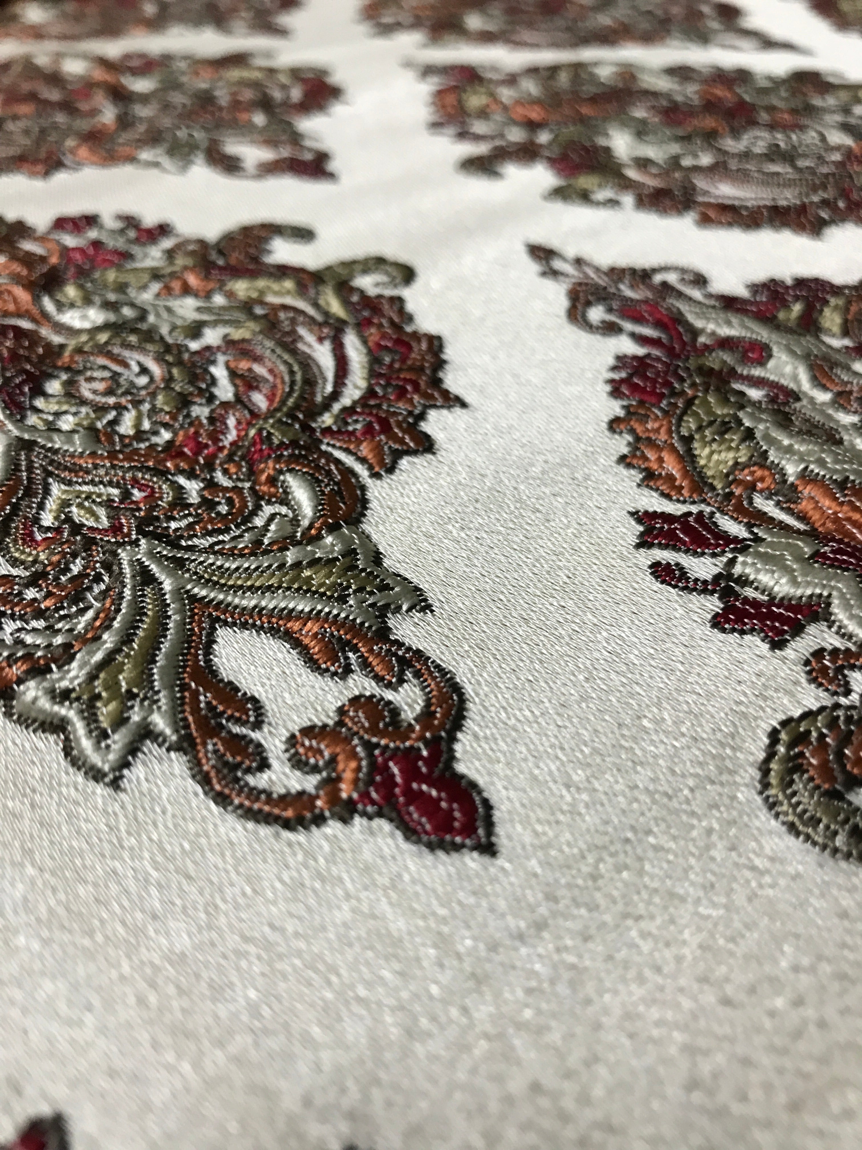 Close-up of embroidered fabric with intricate patterns on a white background  Sage Rose