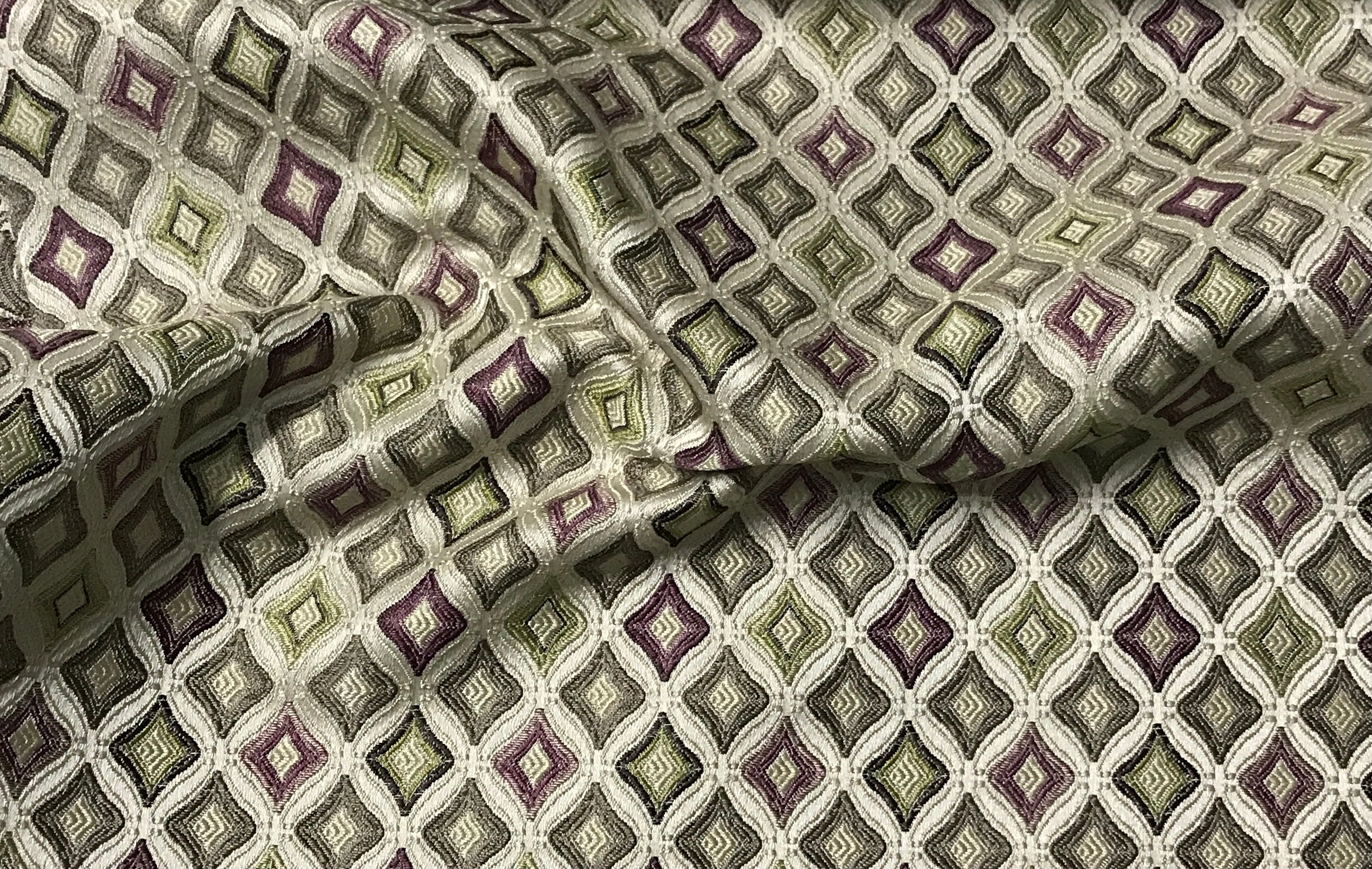 Close-up of patterned fabric with geometric design in green and purple tones. Heritage Sage